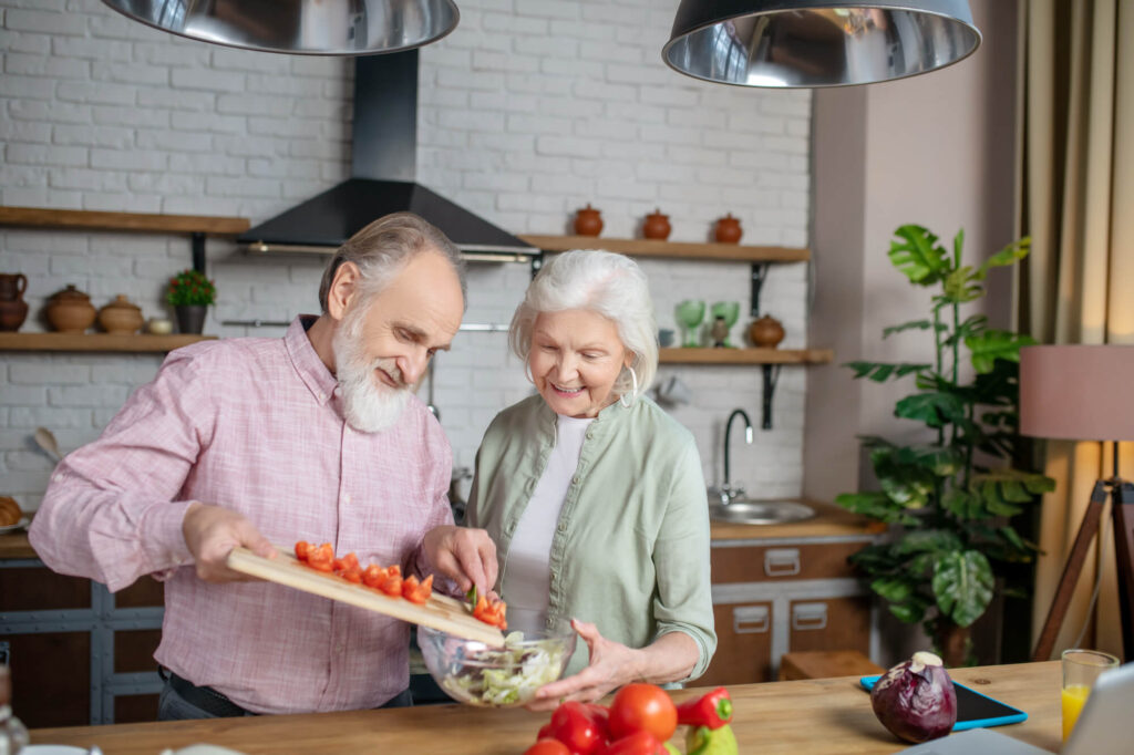 Ernährung im Alter 1 Zwei Senioren schneiden zusammen Tomaten für einen Salat als Symbol für eine gesunde Ernährung im Alter