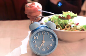 Ein Wecker neben einem Teller mit Essen symbolisiert die Chrono-Ernährung