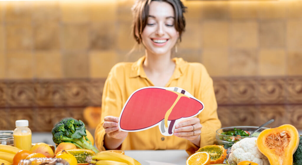 Ernährung bei Lebererkrankungen: Frau mit Lebermodell und leberfreundlichen Lebensmitteln